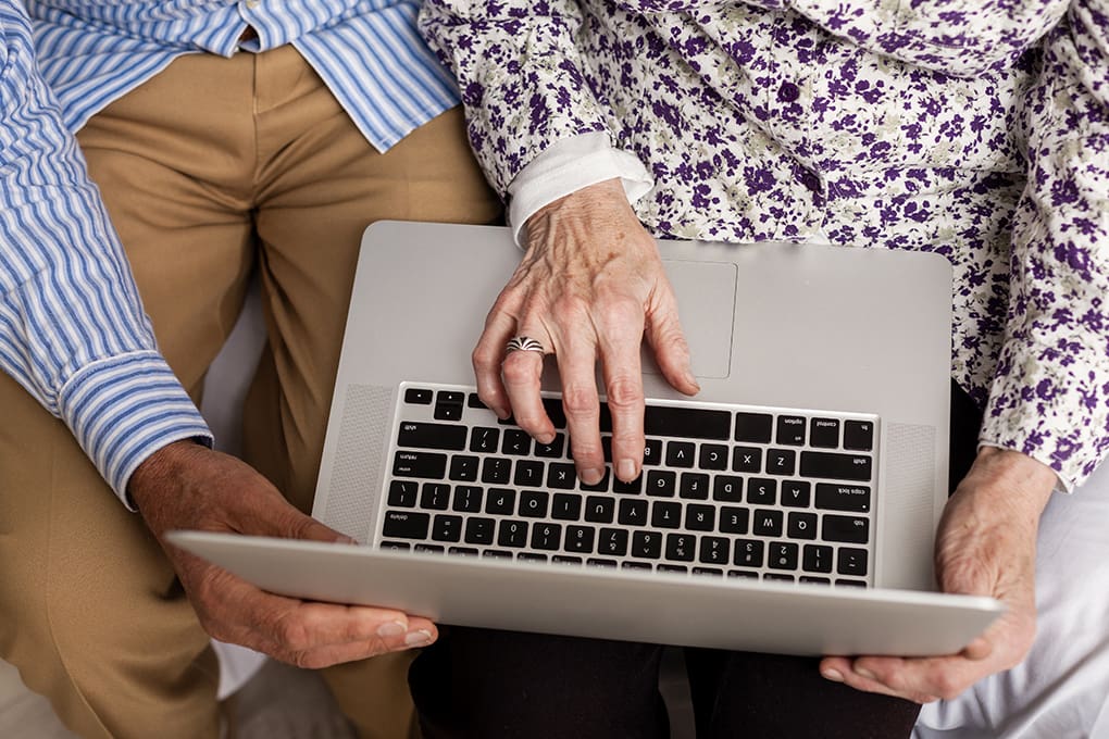 n elderly couple is using a laptop resting on their laps
