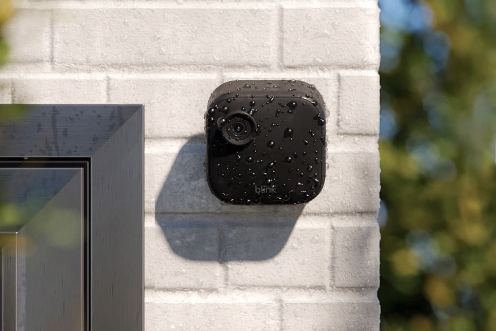 Water-resistant security camera installed on a white brick wall outdoors, covered in raindrops