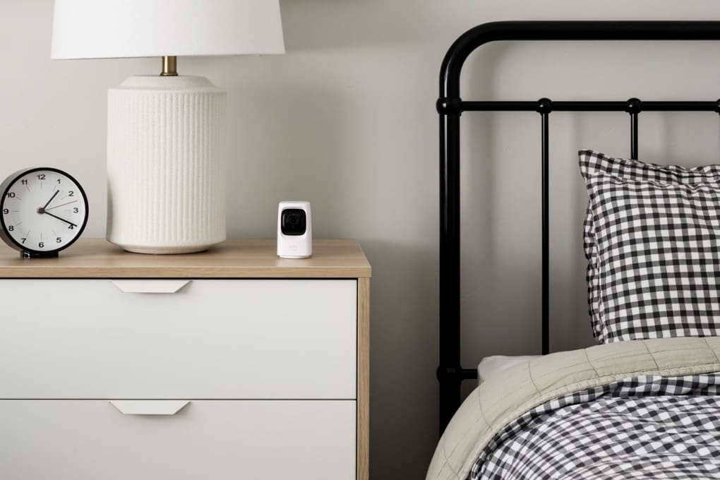 A security camera is kept on a shelf beside a bed and a lamp