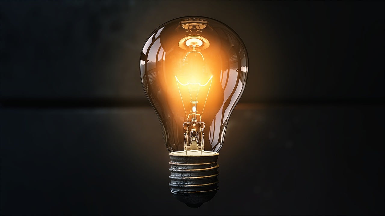 A glowing light bulb against a dark background, emitting a warm orange light