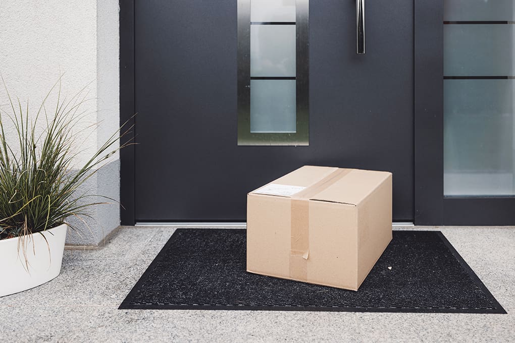 A cardboard package sits on a black doormat in front of a door